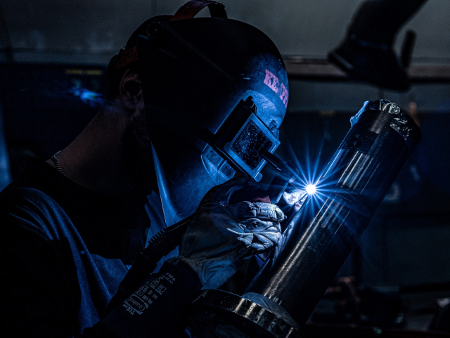 En svetsare i skyddsmask och handskar som svetsar ett metallrör